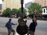 Two men doing air guitar next to giant guitar.
