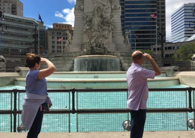 2 team members saluting at an enormous fountain behind them during a team building activity in Indianapolis.