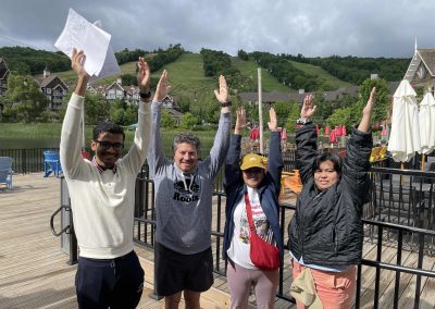 During a team building activity in Collingwood, 4 members stand and pose with their hands raised up.