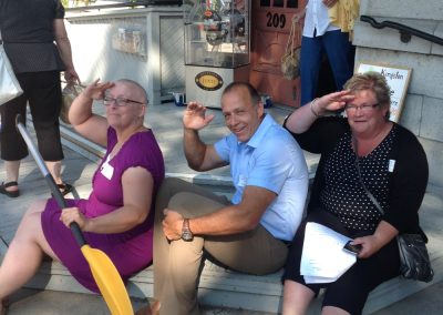 A scavenger hunt team of 3 sitting on a step acting like they are rowing a boat.