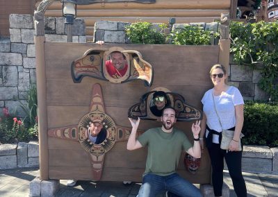 A team of 5, 3 putting their face in a face hole, 2 on their left posing with them during a team building activity in Orlando