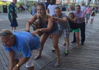 A group of five individuals positioned in a line, leaning forward with their hands placed on the back of the person directly ahead of them during a team building activity in Atlantic City