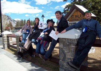 A team of seven people sitting on a fence while smiling during a team building activity in Banff.