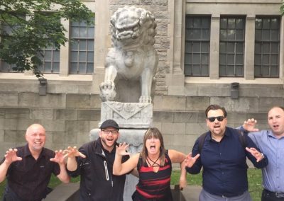 Scavenger hunt team of 5 stands in front of a lion statue, striking a lion roar pose