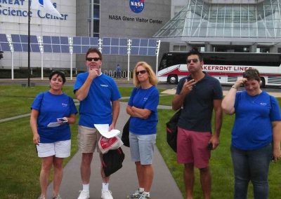 A group of five people standing in front of NASA Glenn Visitor Center, gesturing as if they are thinking during a team building activity in Cleveland.