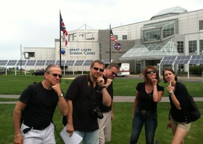 A scavenger hunt team standing in front of the Great Lakes Science Center, gesturing as if they are in deep thought