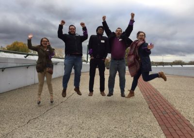 A team of five members jumping, raising their hands and smiling during a team building activity in Grand Rapids.