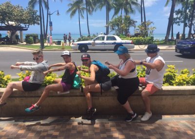 5 people sitting on a seating wall and acting like they are driving a bike