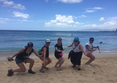 In a beach, five team members bend their knees while looking at the camera