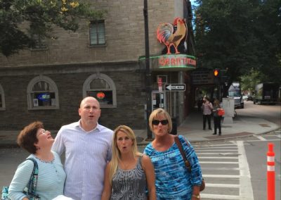 Four people standing in front of a large rooster sign doing a rooster crow during a team building activity in Ithaca