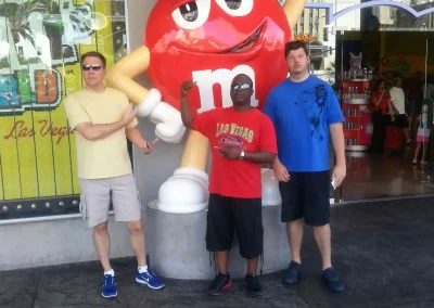 Three people standing in front of a large red m&m's statue and pointing to it