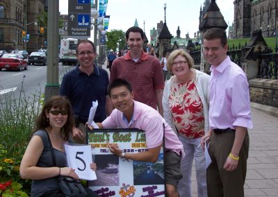 A group of six individuals, with four standing and two seated, posing for a photo alongside a sign during a team building activity in Ottawa.