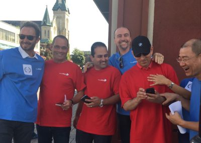 A team of six stands together, with their hands on each other's shoulders. Three of them hold their phones, smiling as they look at the screens.