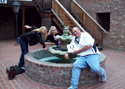 A scavenger hunt team of 3 posing by a fountain, with one in the front arching backward toward the fountain while the two in the back reach down to touch the water.