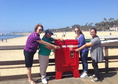 Four women pointing at a fire hose box during the Santa Barbara Scavenger Hunt