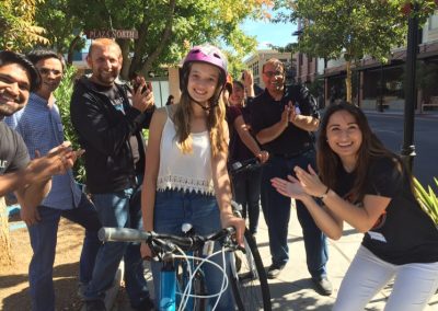 6 scavenger hunt team members clap for a girl in the middle riding a bike.